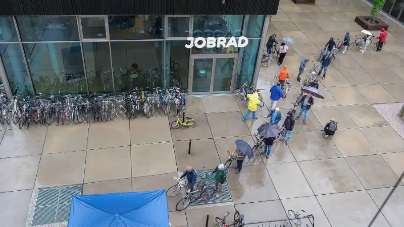 Eine lange Schlange von Menschen mit Fahrrädern und Regenschirmen auf dem JobRad Campus Eine lange Schlange von Menschen mit Fahrrädern und Regenschirmen auf dem JobRad Campus