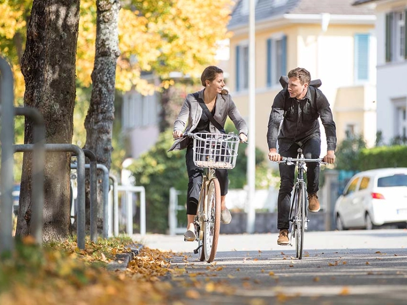 Zwei Radfahrer:innen fahren im Herbst zusammen Fahrrad